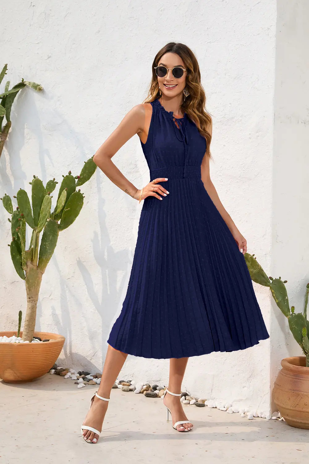 Woman wearing a navy blue dress standing in front of a white wall with cacti.