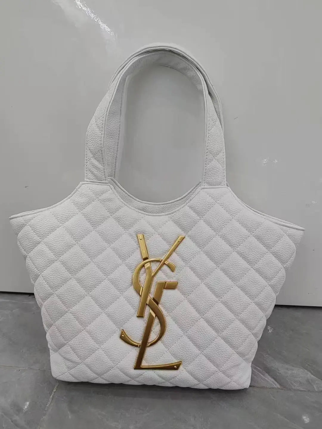 White quilted handbag with gold logo on a gray surface