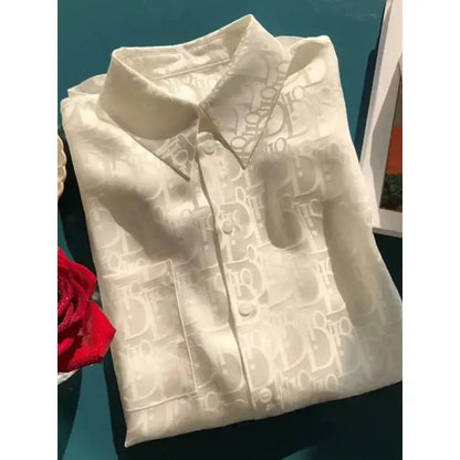 Folded white shirt with brand logo on a teal surface next to a red rose