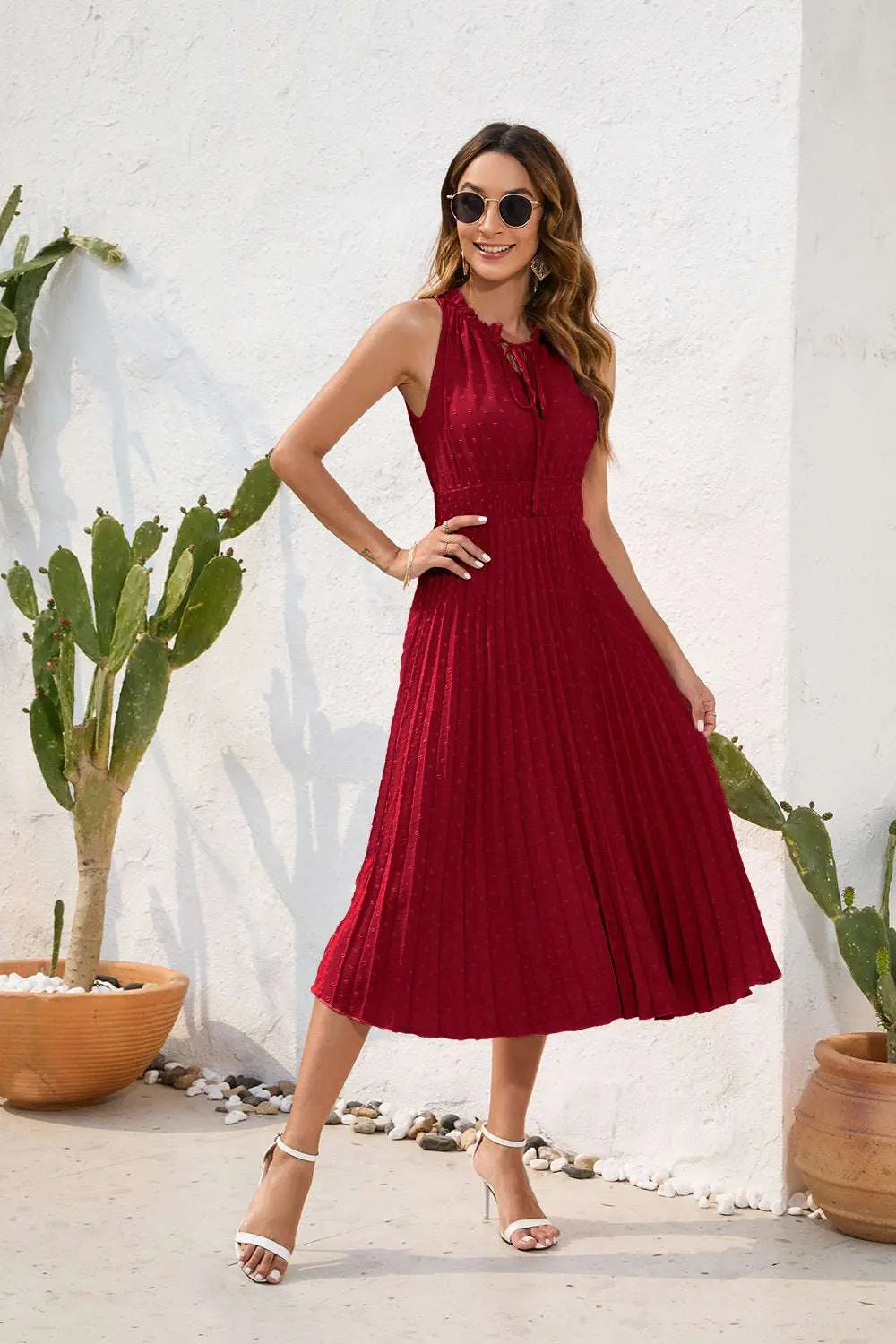 Woman in a red dress standing outdoors with plants and a white wall in the background