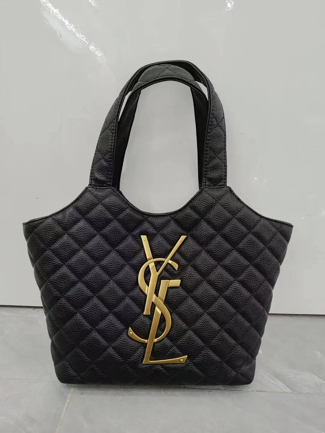 Black quilted handbag with gold logo on a light gray background